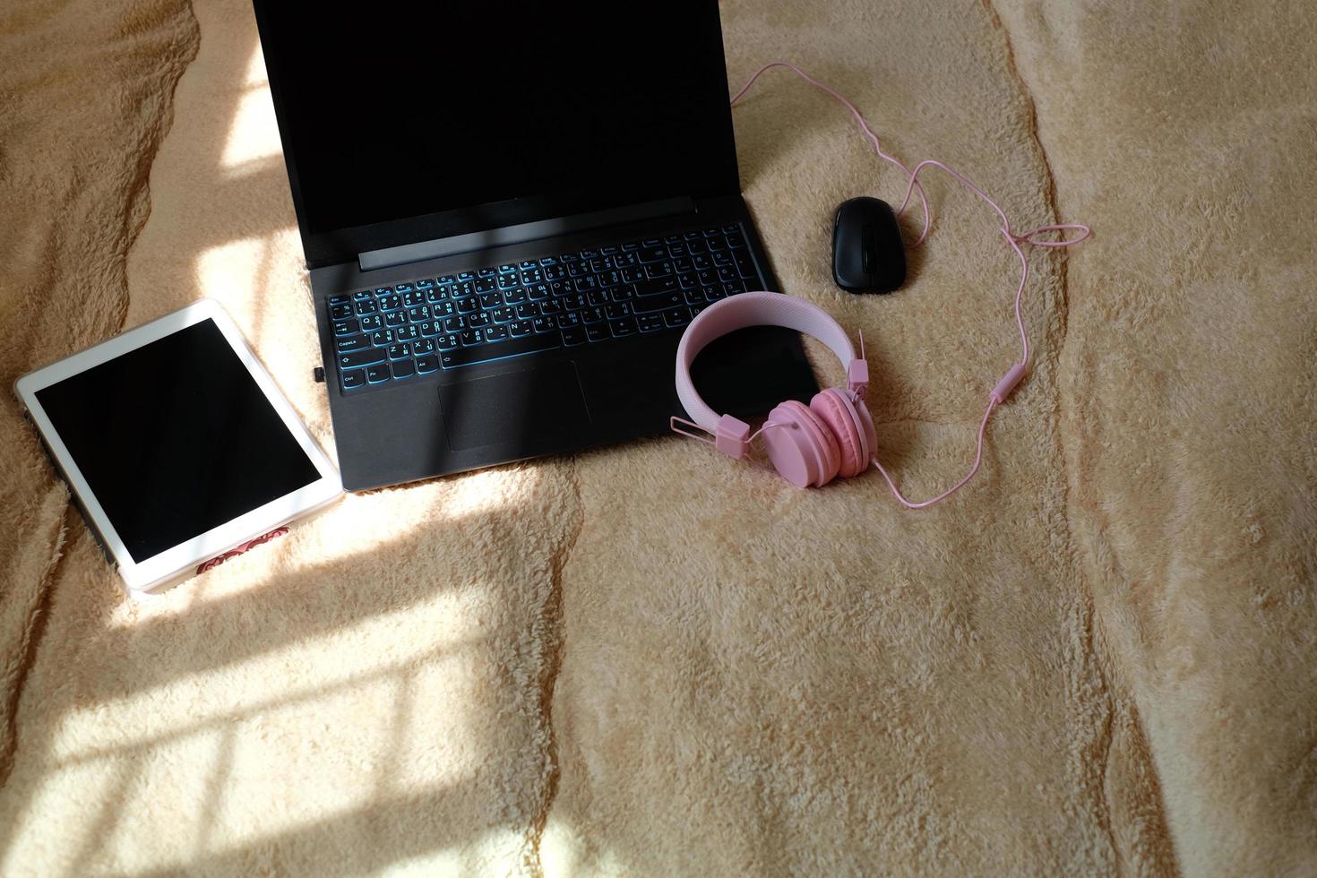 A laptop computer, digital tablet and headphones on the bed for using electronics during quarantine. workspace at home with the morning light. The concept of work at home and online education.Flat lay photo