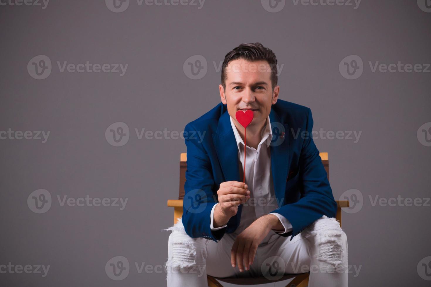 Happy man with red heart shape against gray background. photo