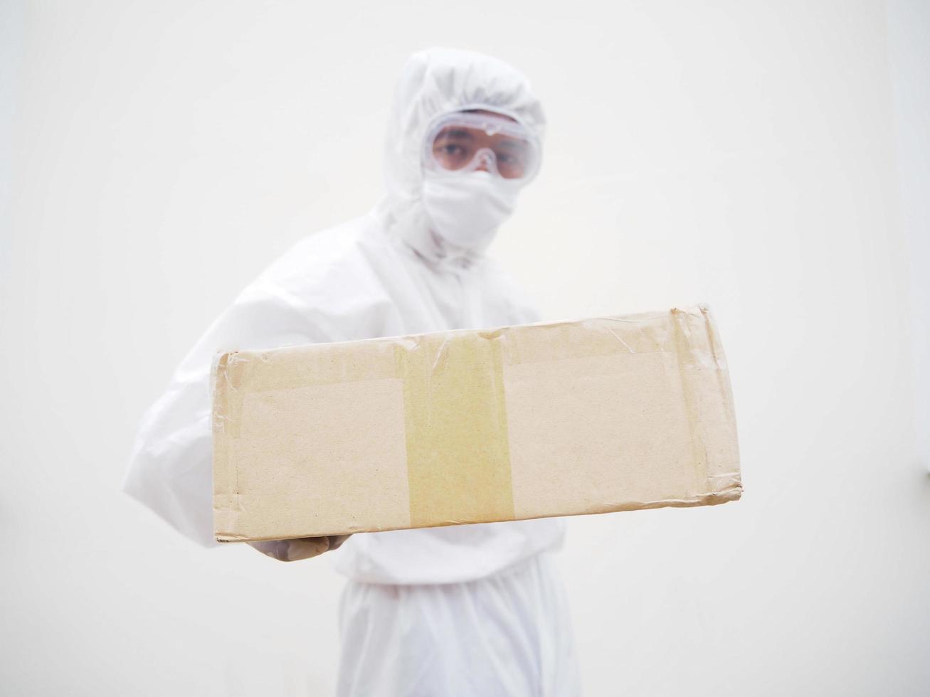 joven con uniforme de suite de ppe mientras sostiene cajas de cartón con guantes médicos de goma y máscara. concepto de coronavirus o covid-19 fondo blanco aislado foto