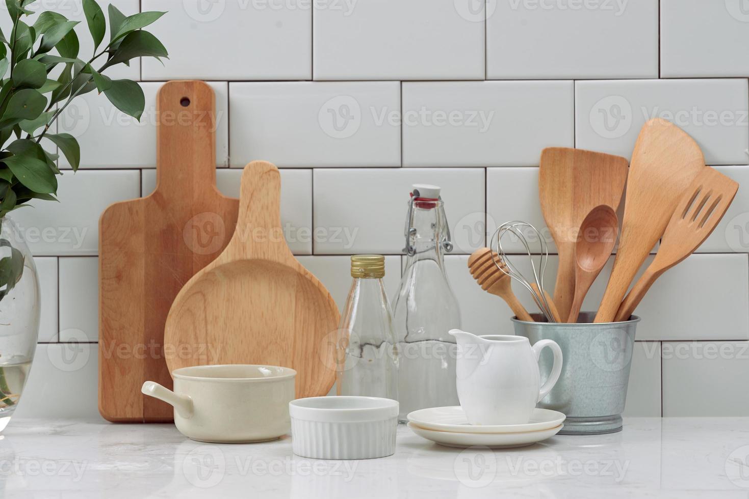 Simple rustic kitchenware against white wooden wall rough ceramic pot with wooden cooking utensil set, stacks of ceramic bowls, jug and wooden trays. photo