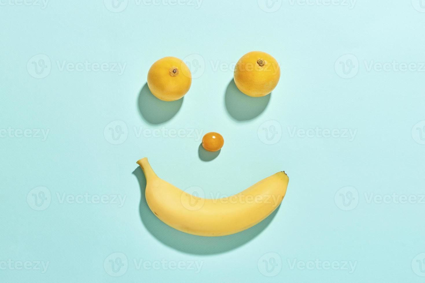 Happy fruit face with banana, tomato and lemons isolated on blue background photo
