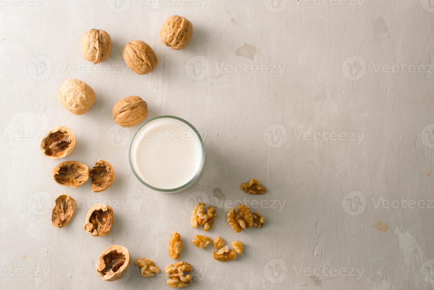 Organic walnut nuts and glass of walnut milk on stone background. photo