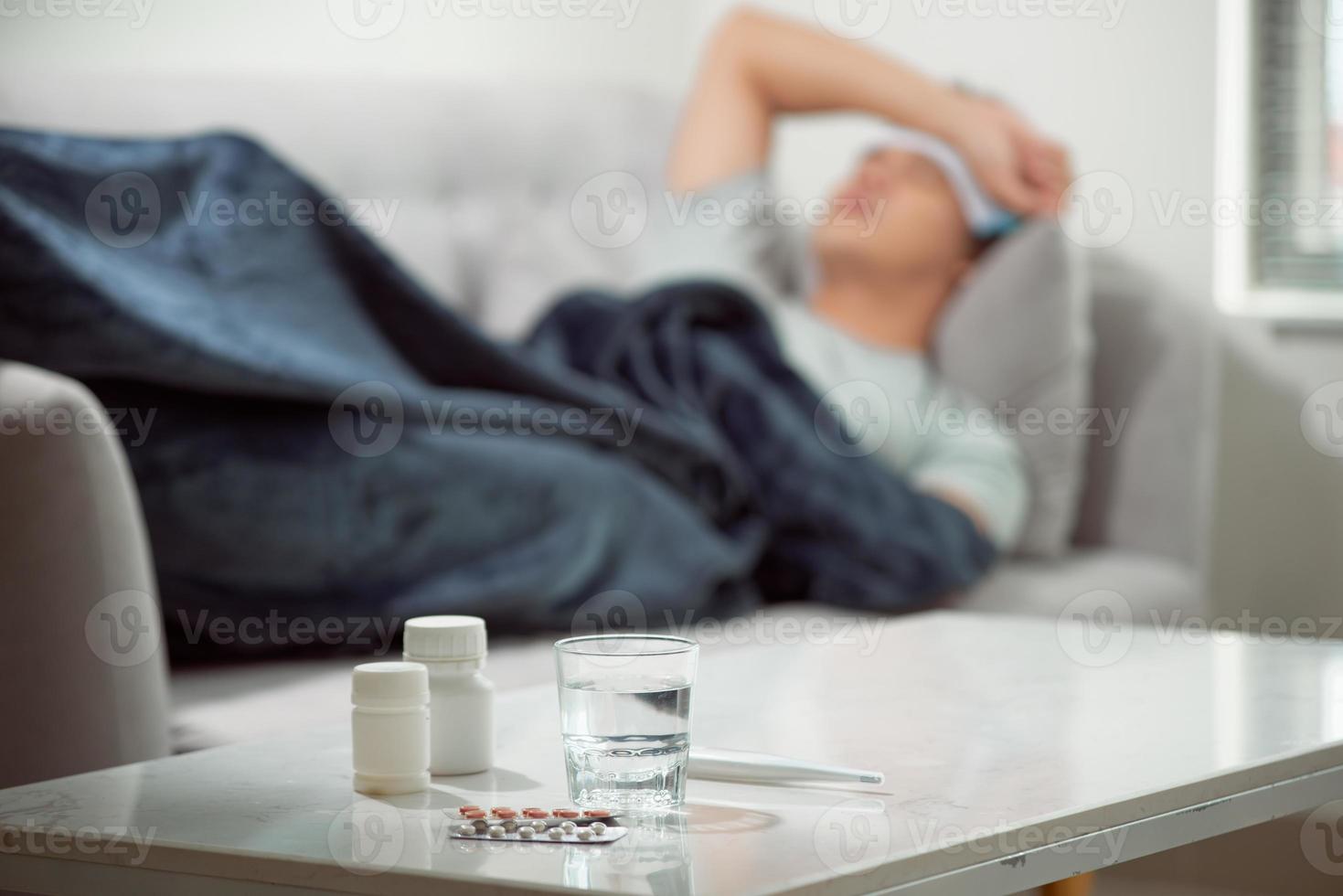 sick wasted man lying in sofa suffering cold and winter flu virus having medicine tablets in health care concept looking temperature on thermometer photo