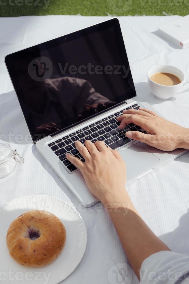 hombre de las manos en el teclado de la computadora portátil y café con donut. estilo de vida de trabajo fácil en casa por la mañana. foto