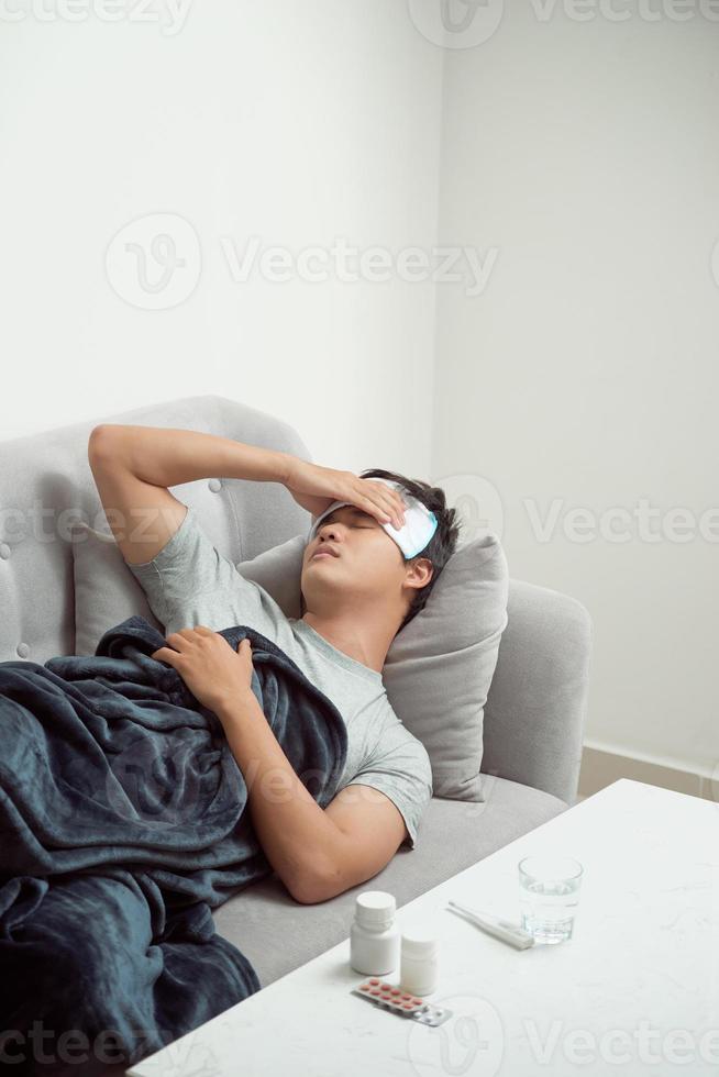 sick wasted man lying in sofa suffering cold and winter flu virus having medicine tablets in health care concept looking temperature on thermometer photo
