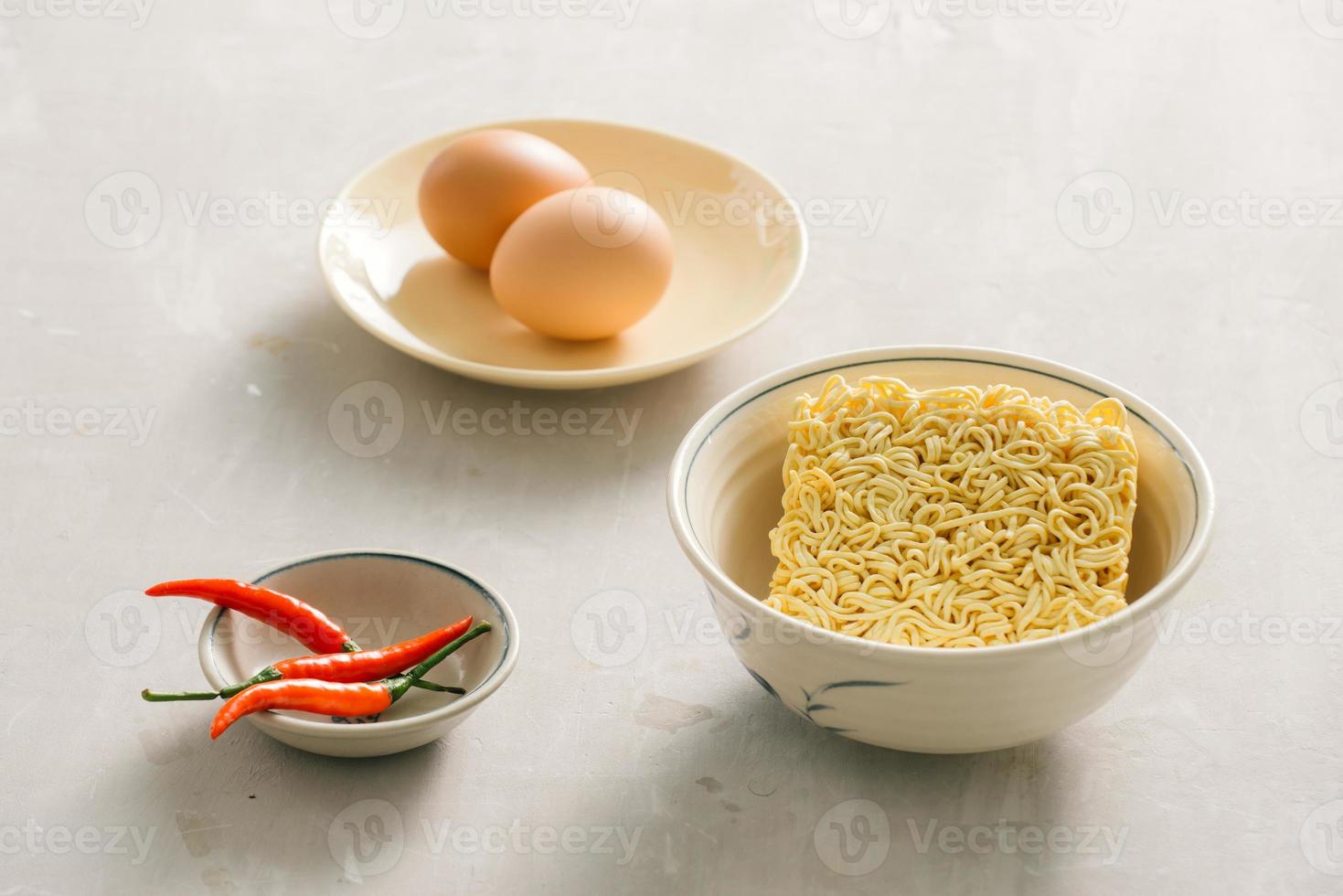 Instant noodles in bowl and vegetable side dishes on stone background. Quick and easy food concept. photo