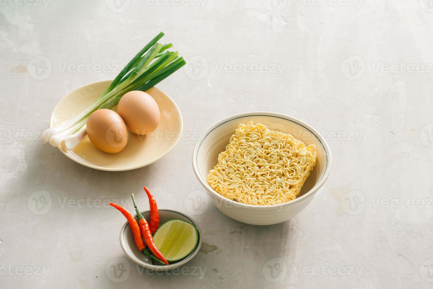 Instant noodles in bowl and vegetable side dishes on stone background. Quick and easy food concept. photo