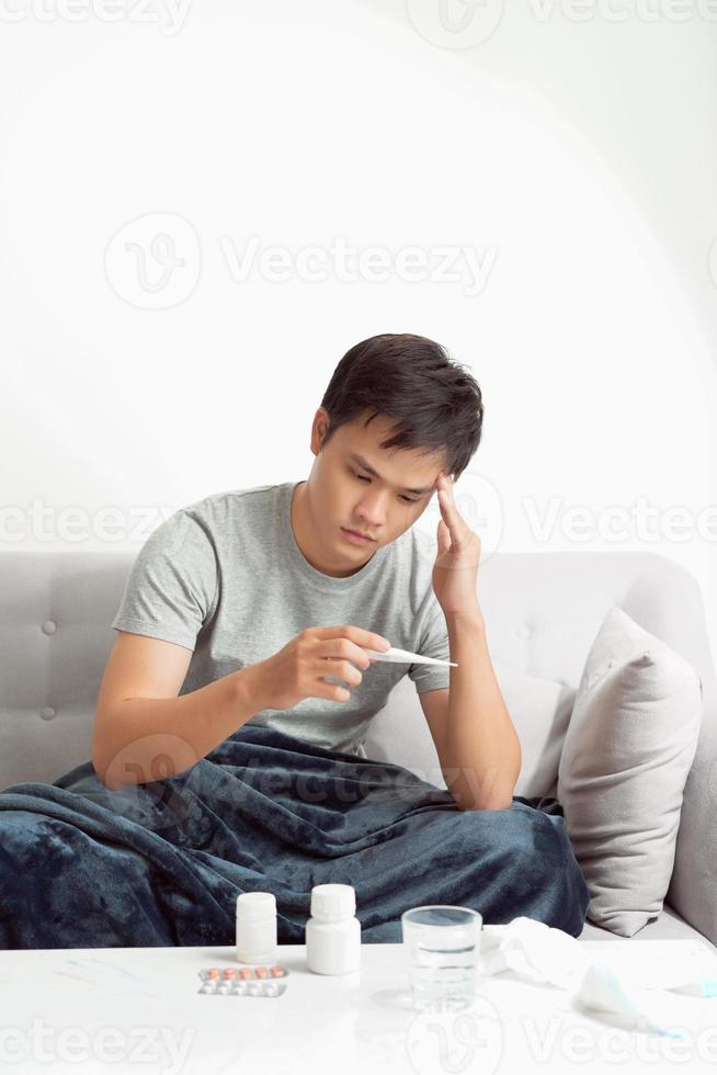 Sick man lying on sofa checking his temperature at home in the living room photo