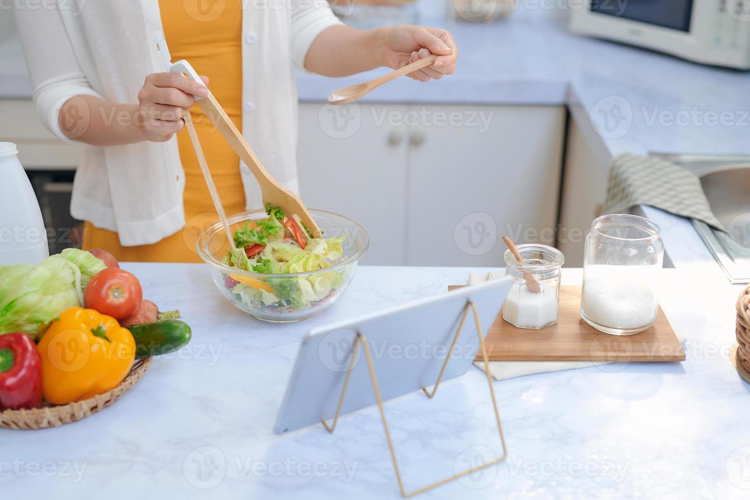 Subject shot of female hand holding stainless steel kitchen tongs with salad leaves above glass bowl. photo