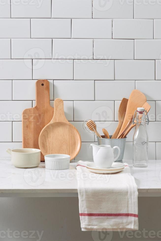 Simple rustic kitchenware against white wooden wall rough ceramic pot with wooden cooking utensil set, stacks of ceramic bowls, jug and wooden trays. photo