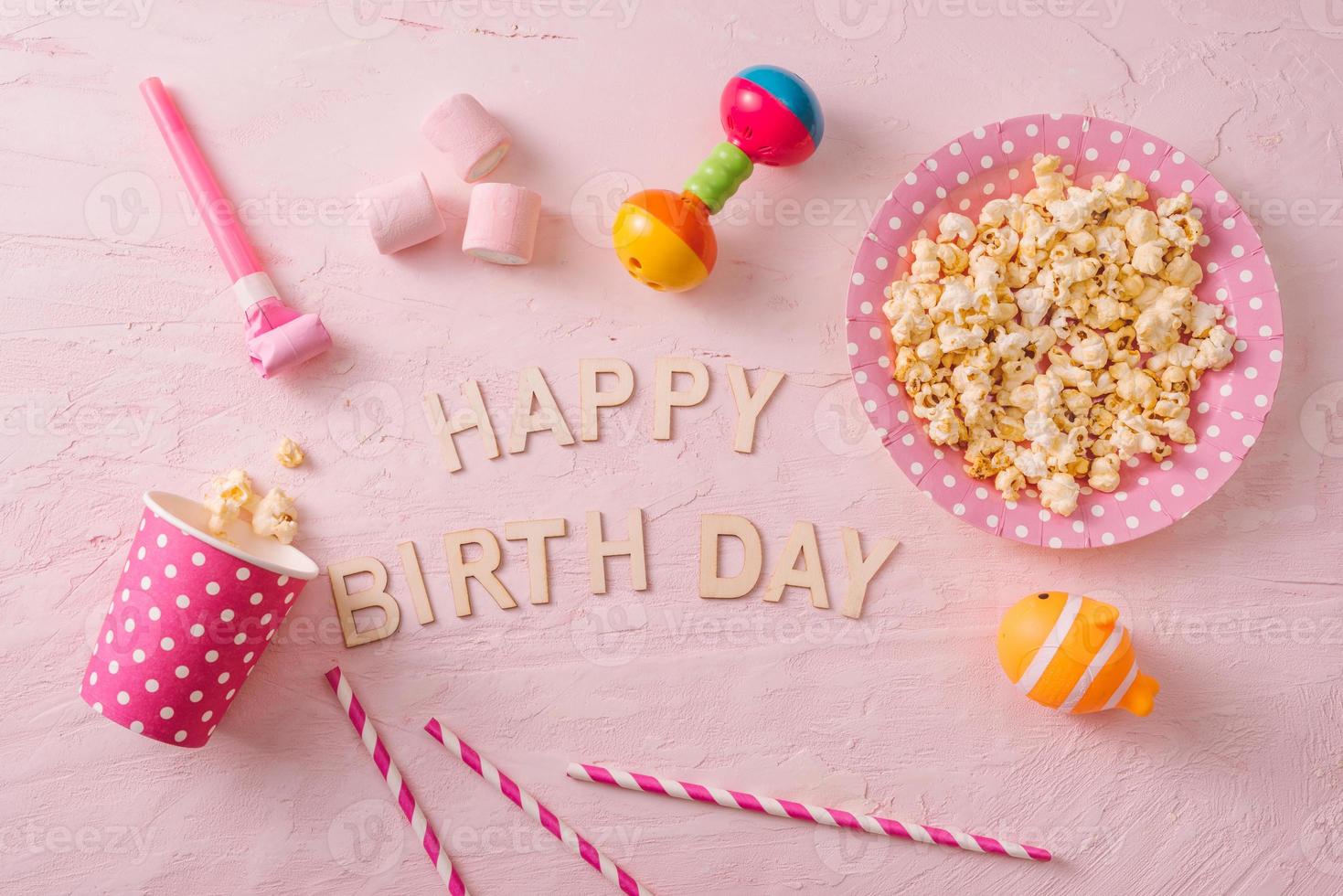 Birthday party background, border of confetti, sweets, lollipops and gift on pink surface, copy space, top view photo