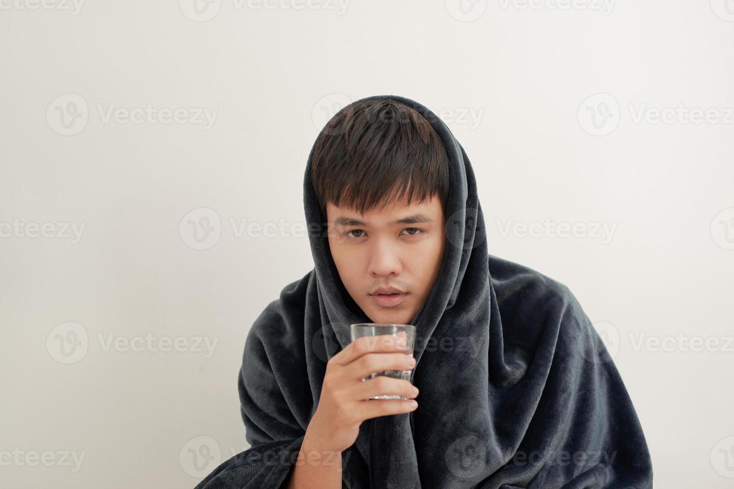 A young man is sick with flu, lies at home under a blanket, takes a pill photo