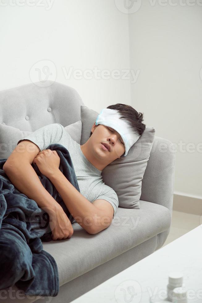 Sick man lying on sofa checking his temperature under a blanket at home in the living room photo