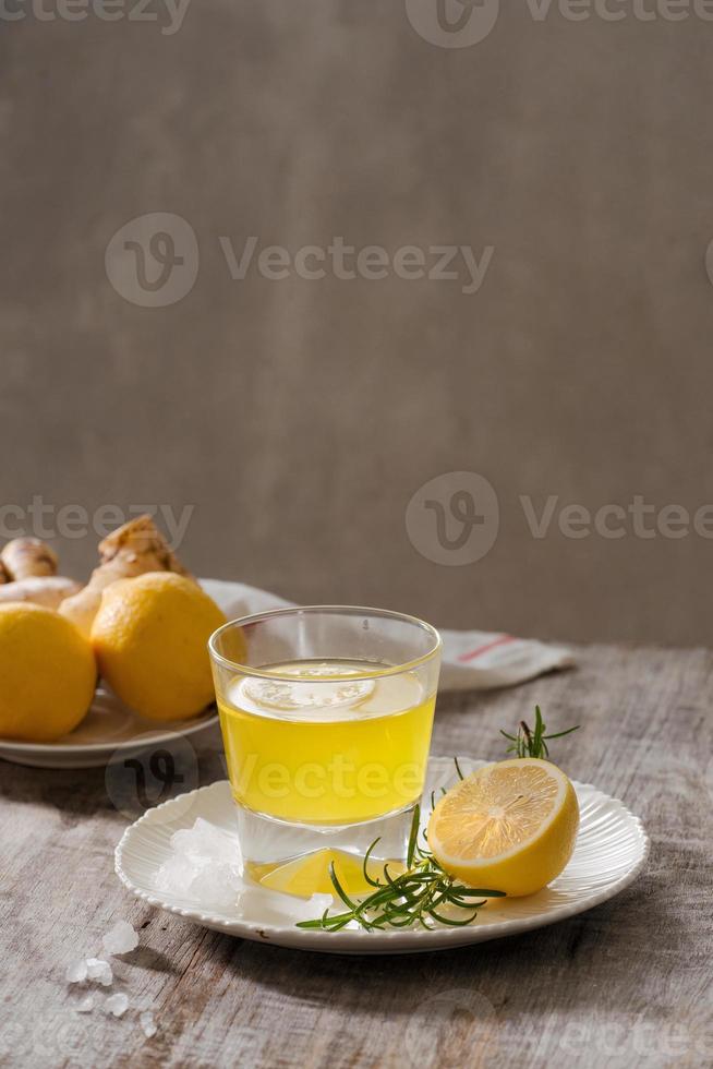 Ginger tea with lemon, ginger root and rosemarry on wooden background. Small glass transparent pitcher with hot drink. Seasonal beverages. Shallow DOF, selective focus, focus on top of pitcher. photo