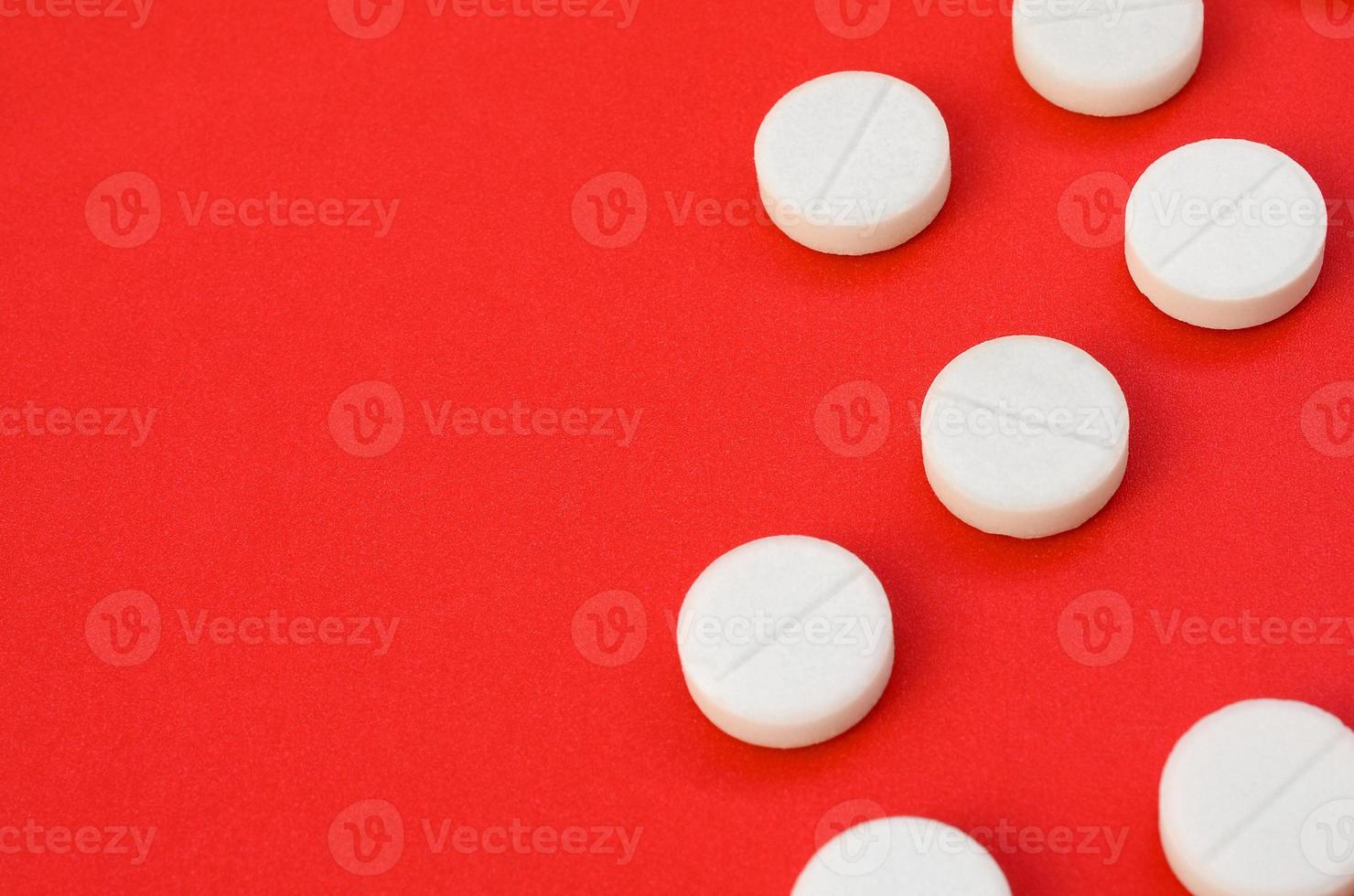 A few white tablets lie on a bright red background surface. Background image on medical and pharmaceutical topics photo