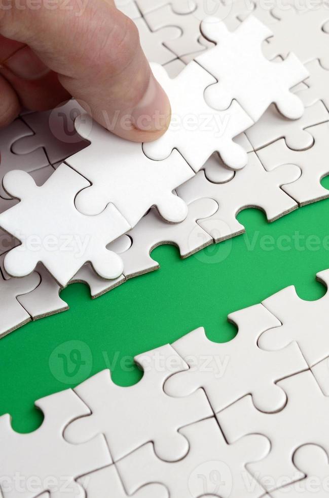 The human hand paves the way to the surface of the jigsaw puzzle, forming a green space. The concept of overcoming the difficulties on the way to success photo