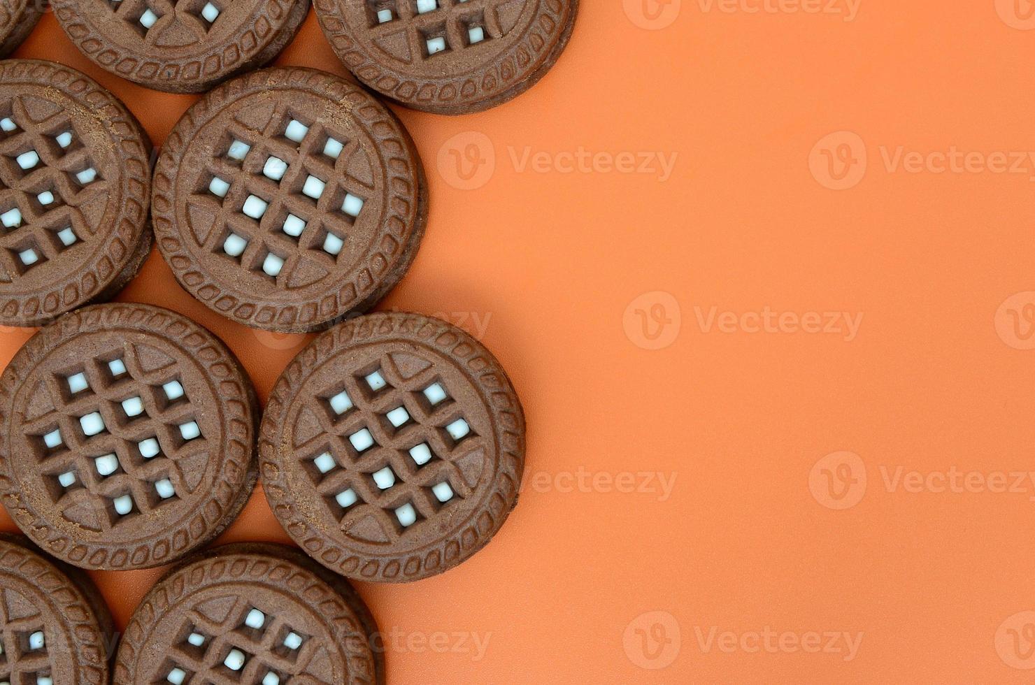 Detailed picture of dark brown round sandwich cookies with coconut filling on an orange surface. Background image of a close-up of several treats for tea photo