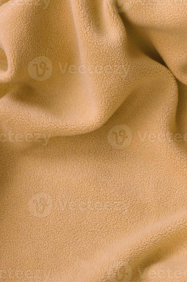 The blanket of furry orange fleece fabric. A background of light orange soft plush fleece material with a lot of relief folds photo
