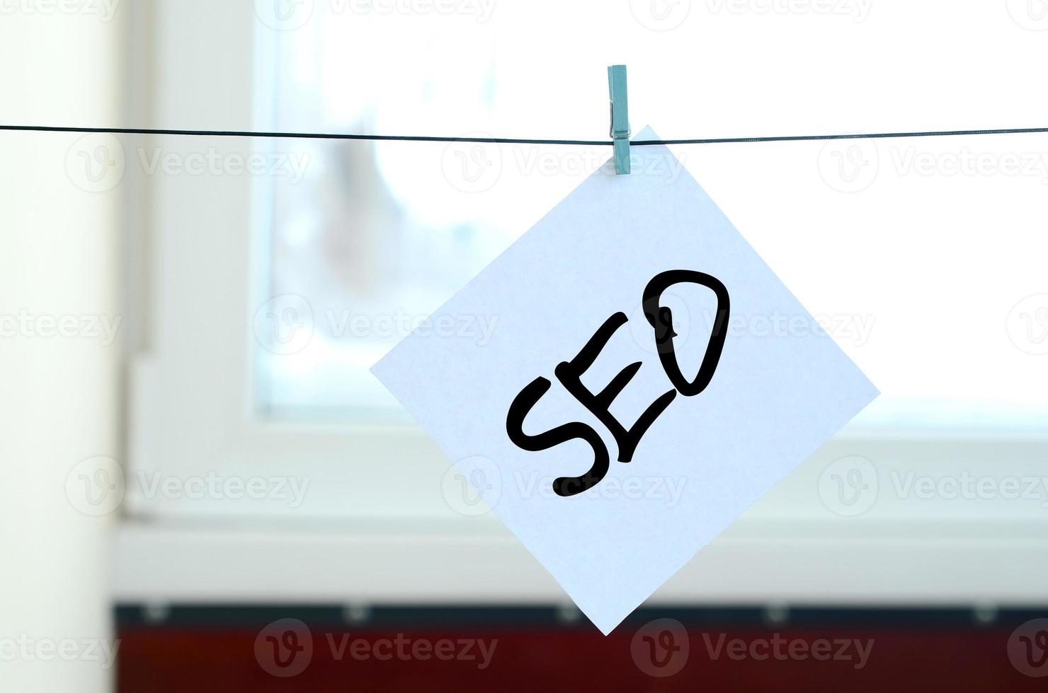 SEO. Note is written on a white sticker that hangs with a clothespin on a rope on a background of window glass photo