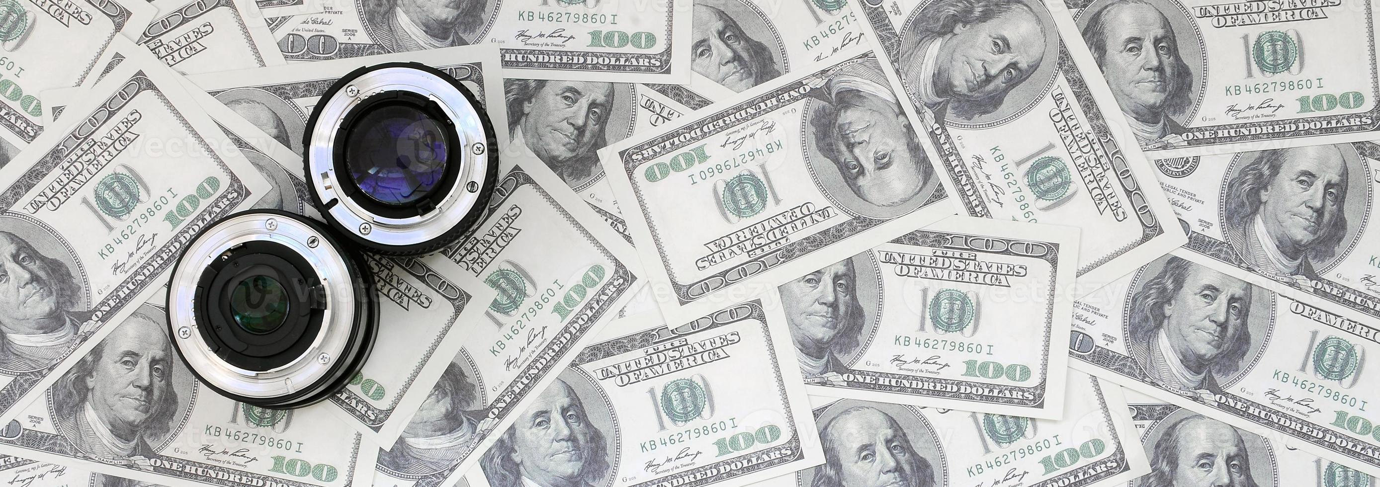 Two photographic lenses lie on the background of a lot of dollar bills. Space for text photo