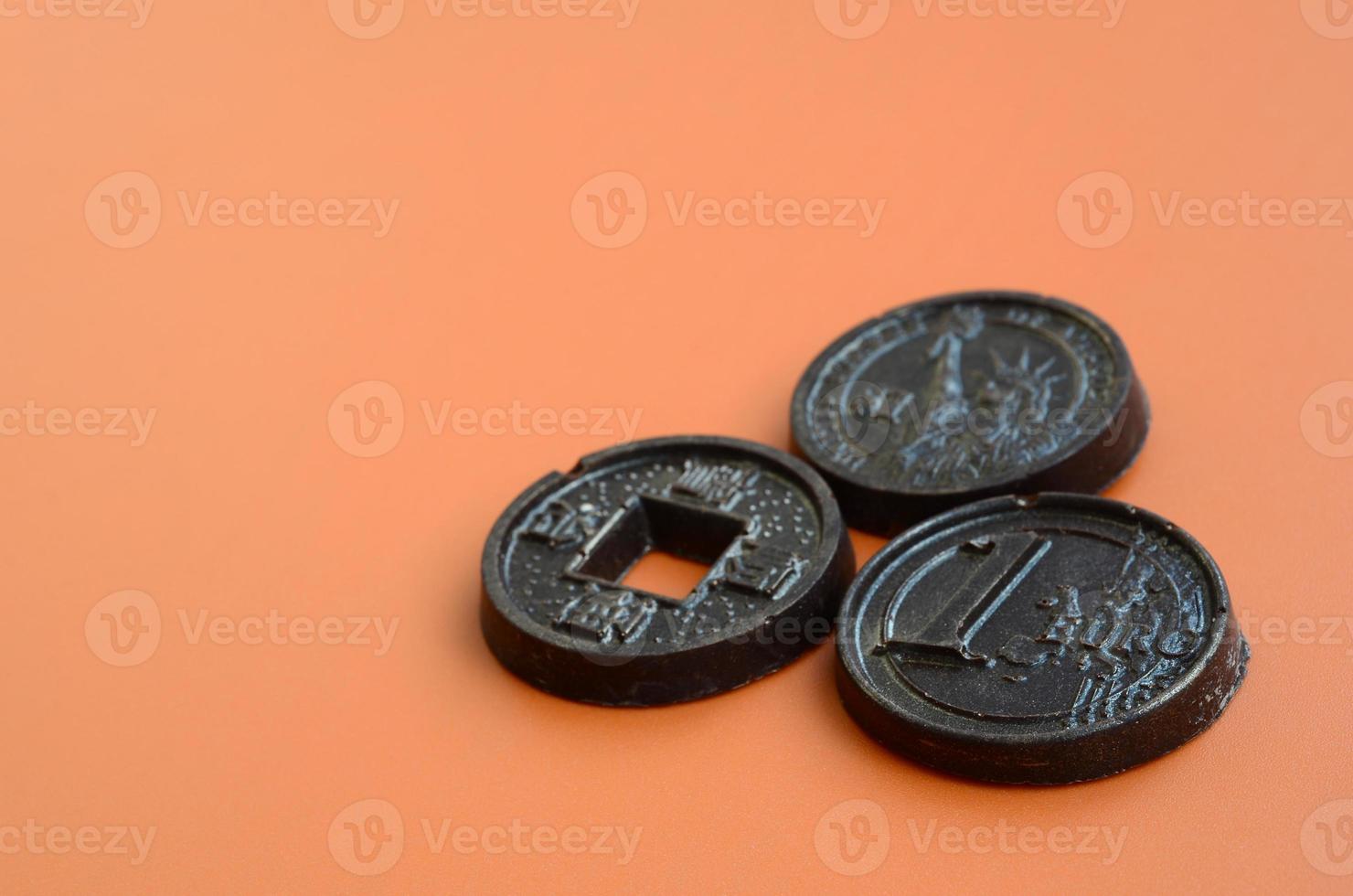 Three chocolate products in the form of Euro, USA and Japan coins lie on an orange plastic background. A model of cash coins in an edible form photo