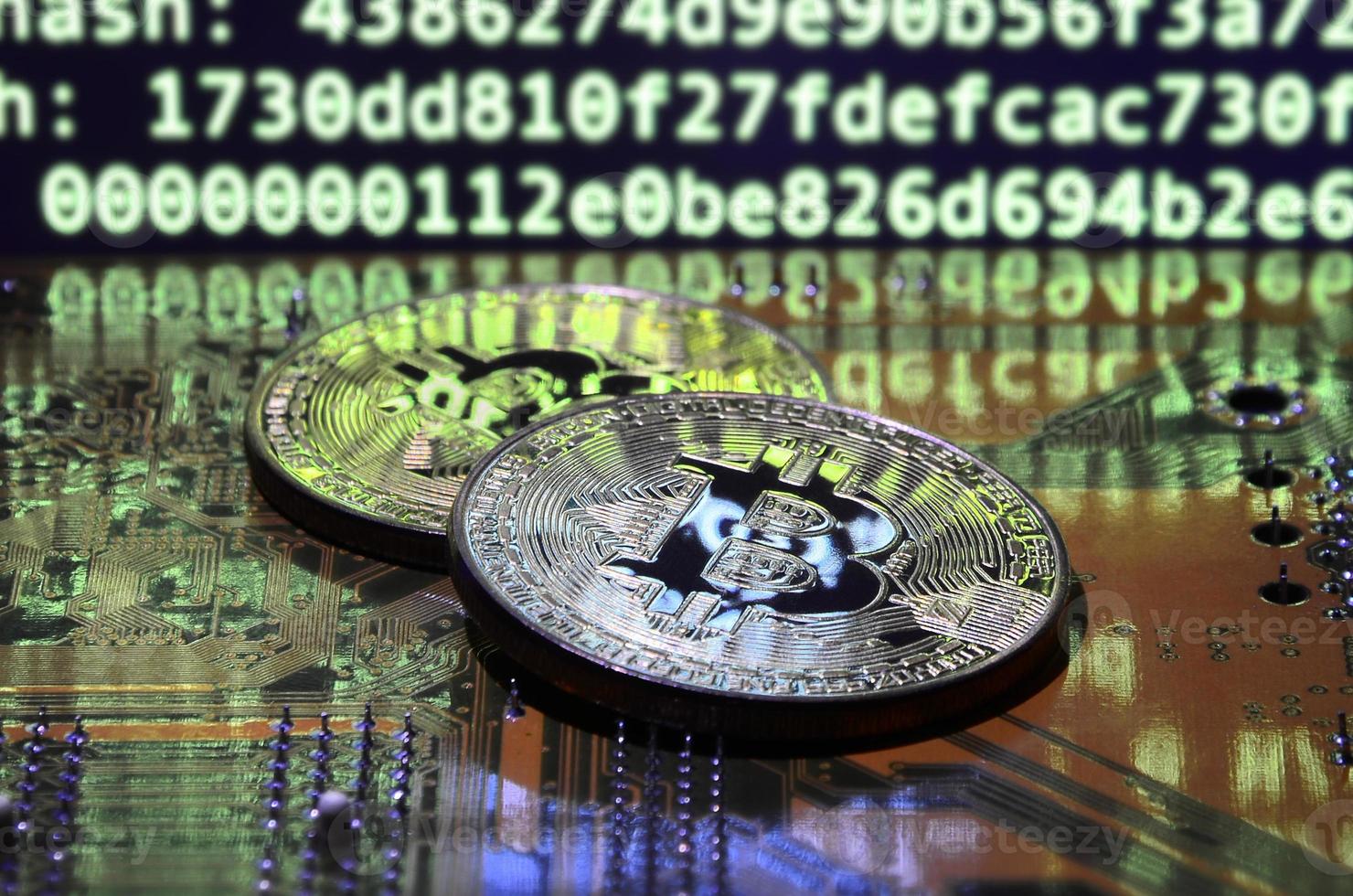 Two bitcoins lies on a videocard surface with background of screen display of cryptocurrency mining by using the GPUs photo