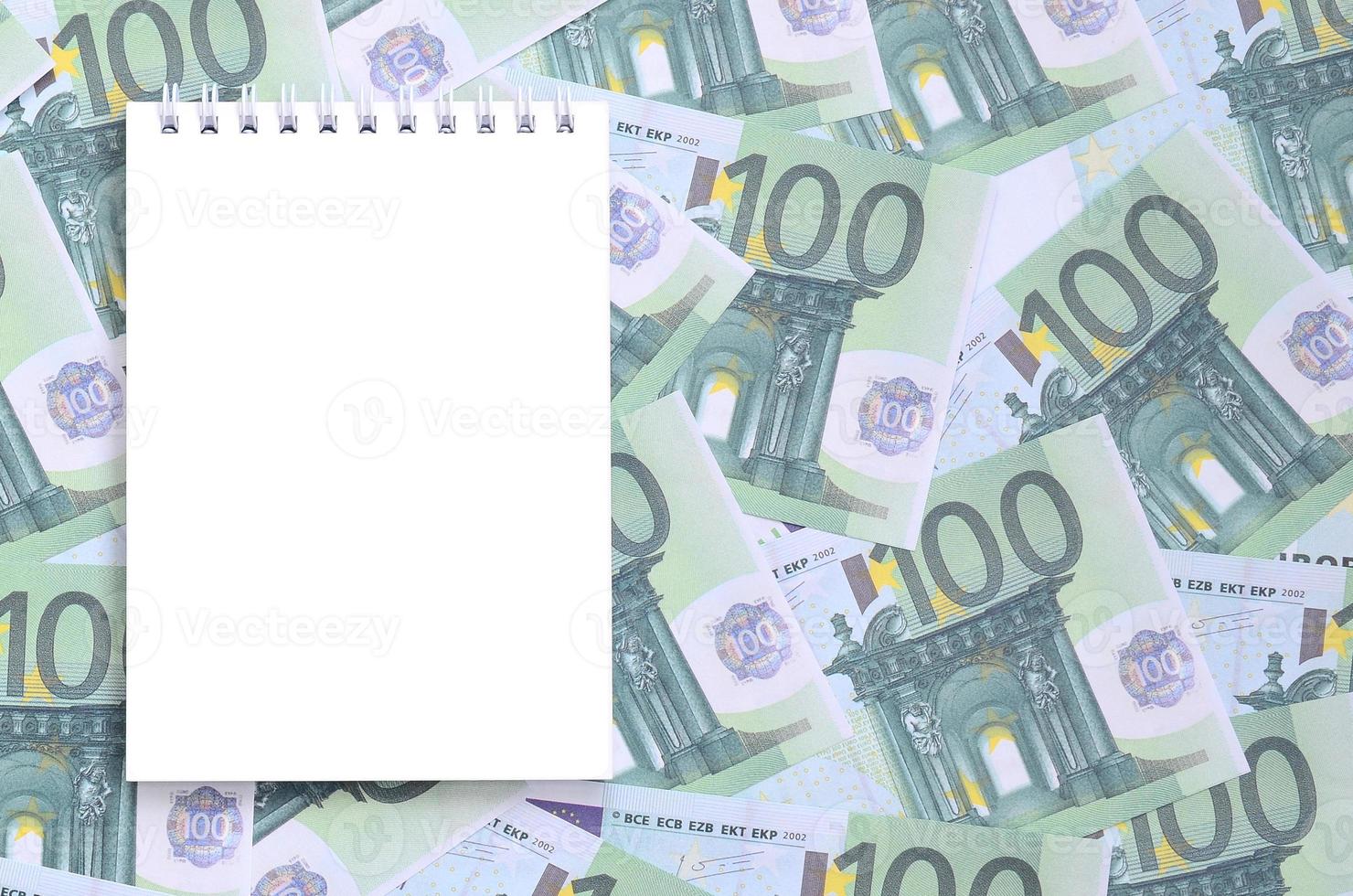 cuaderno blanco con páginas limpias sobre un conjunto de denominaciones monetarias verdes de 100 euros. mucho dinero forma un montón infinito foto