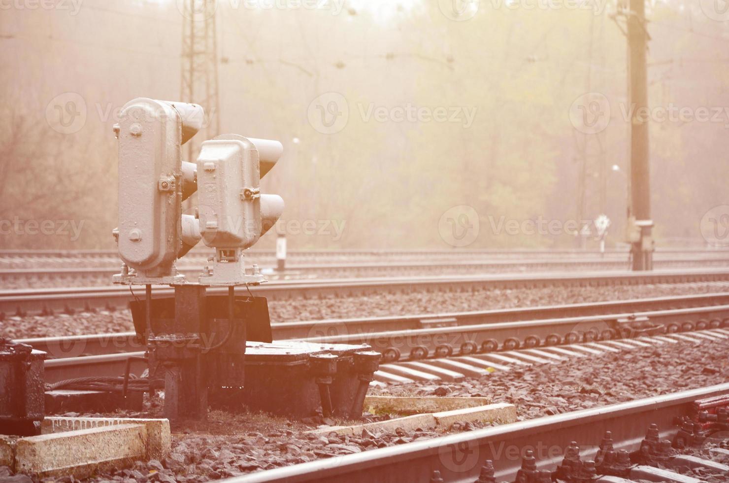 Photo of a fragment of a railway track with a small traffic light in rainy weather