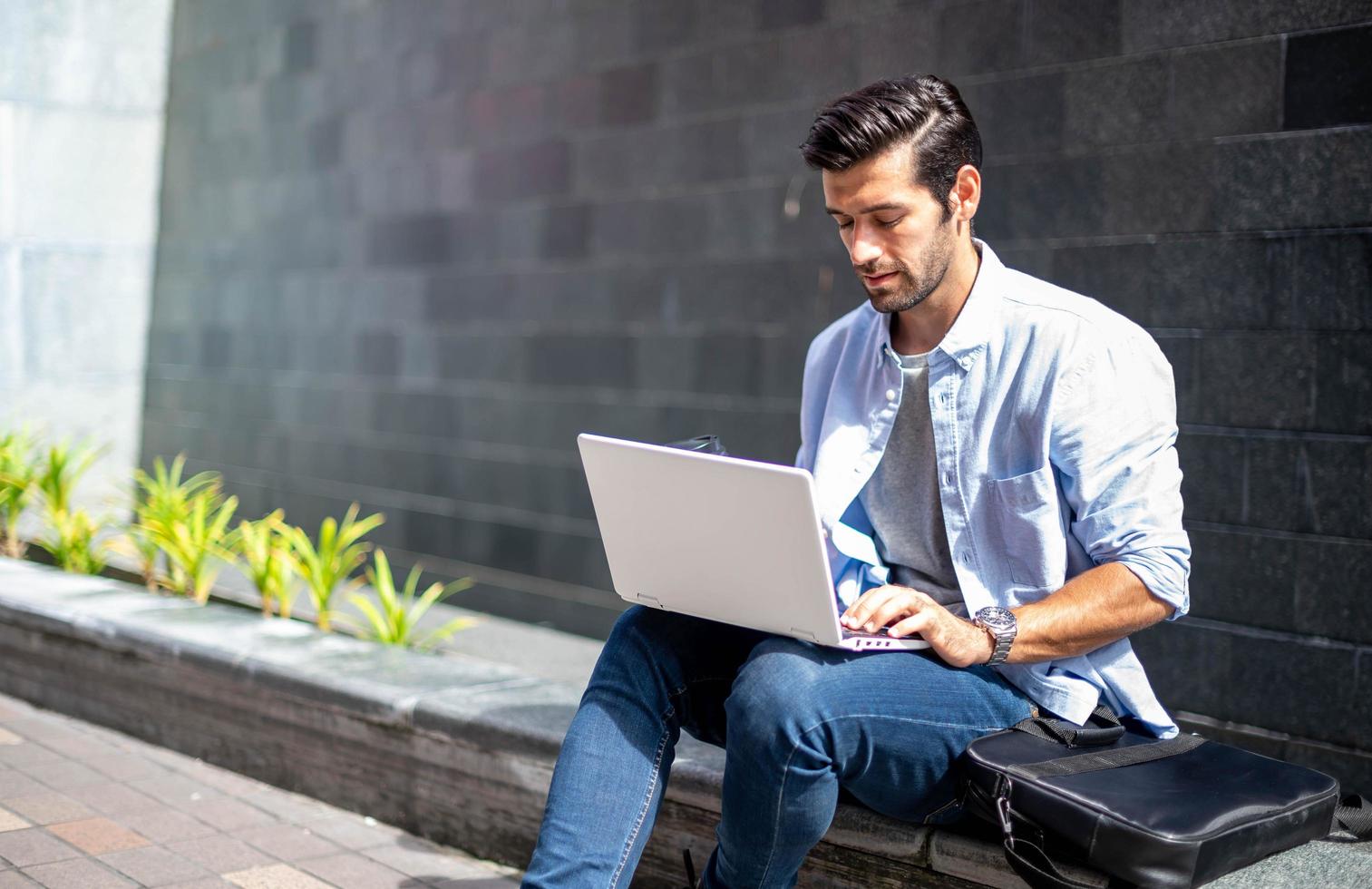 Young caucasian man sitting and working on freelance project using portable computer at outer office. photo