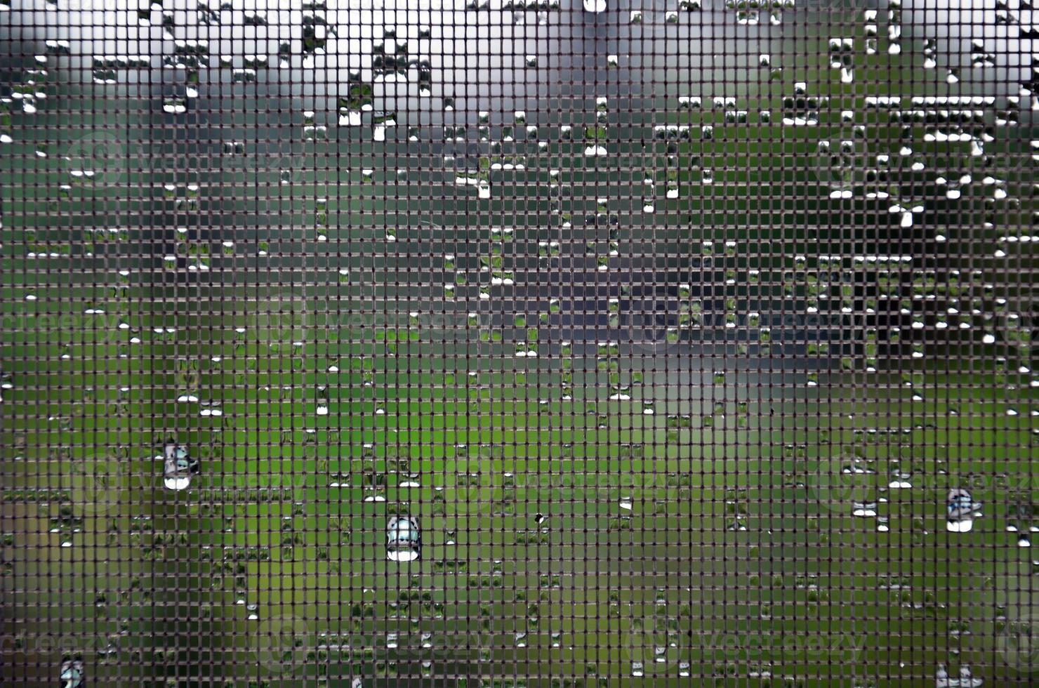 Background image of rain drops on a glass window, which is protected by a mosquito net. Macro photo with shallow depth of field