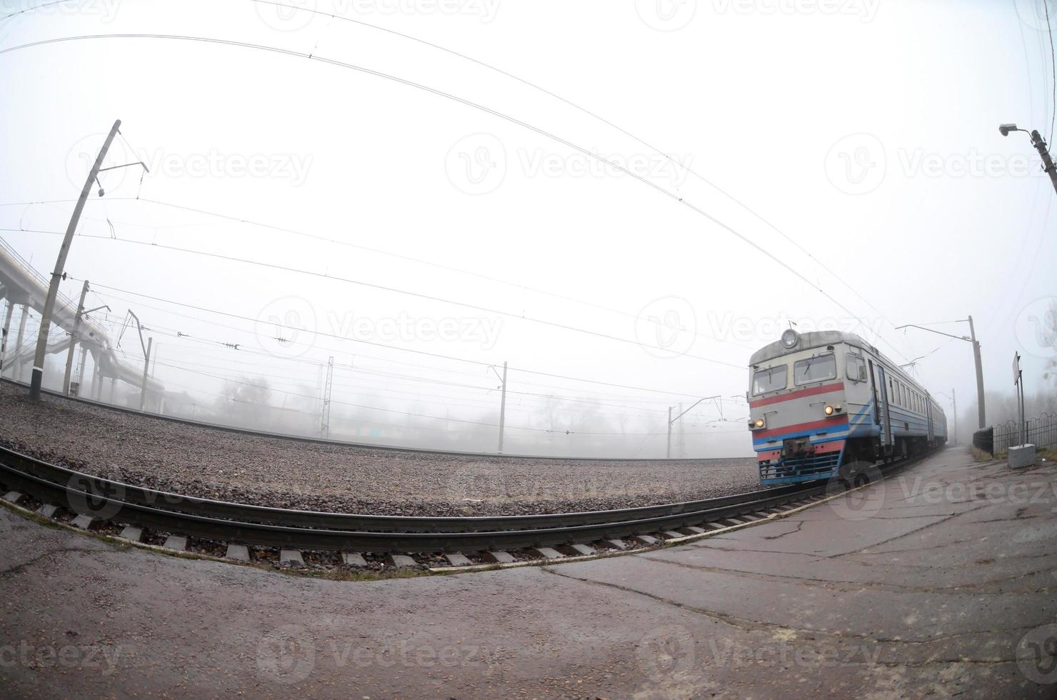 The Ukrainian suburban train rushes along the railway in a misty morning. Fisheye photo with increased distortion