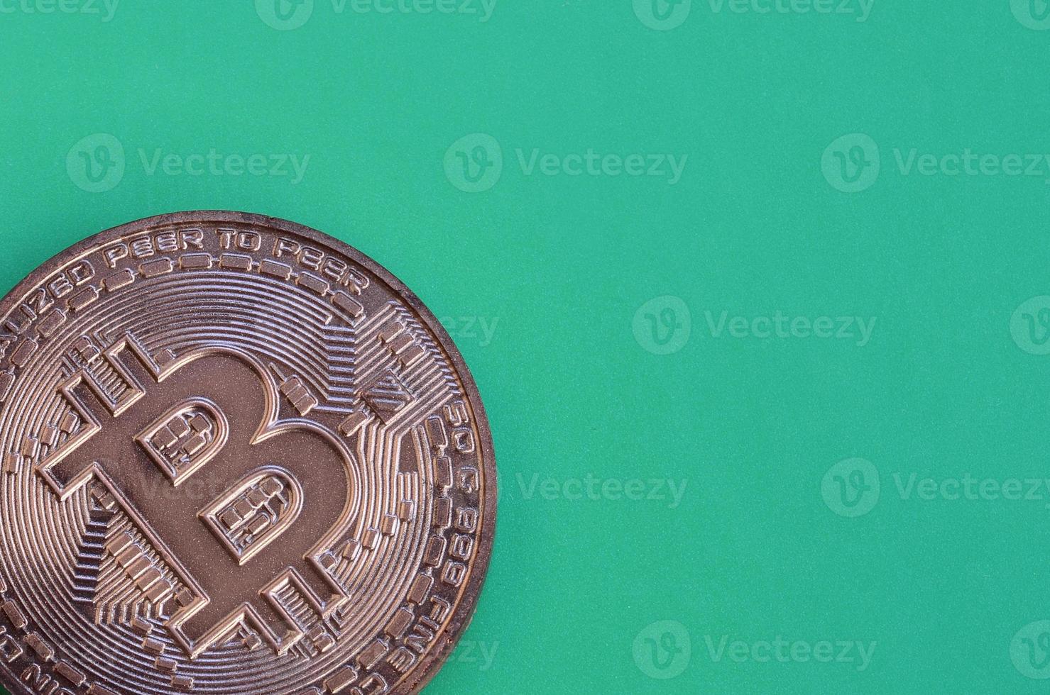 Chocolate product in the form of physical bitcoin lies on a green plastic background. Model of the crypto currency in the edible form photo