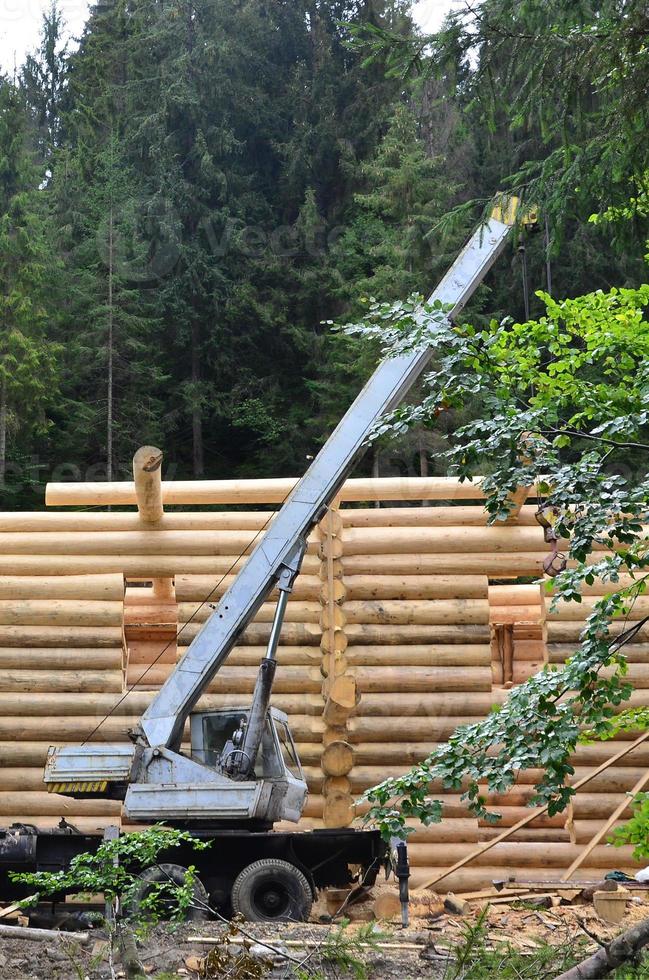 el proceso de construcción de una casa de madera a partir de vigas de madera de forma cilíndrica. grúa en condiciones de trabajo foto