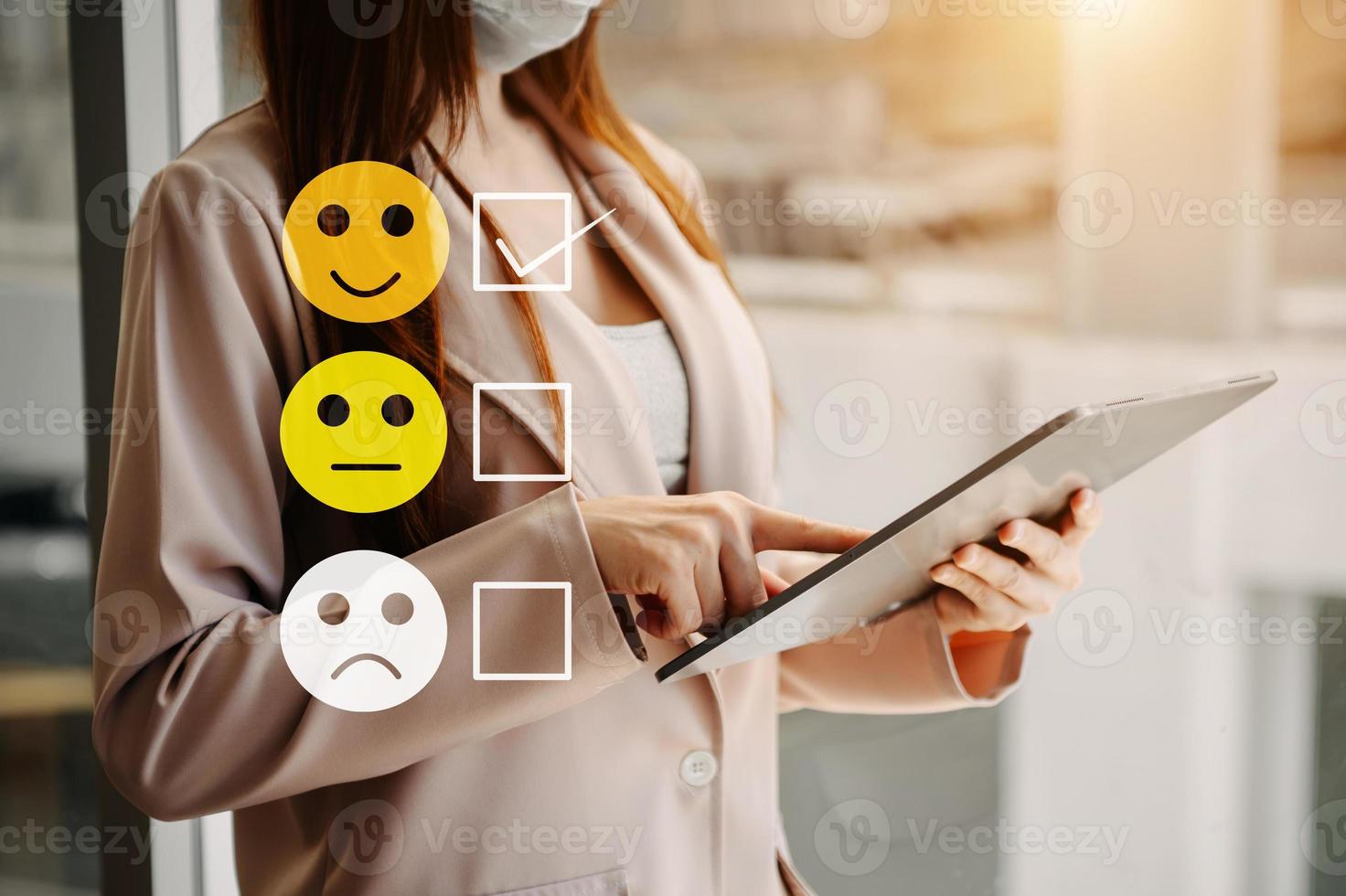 Customer service evaluation concept. woman Show face smile emoticon show on virtual screen from hand.looking at tablet and laptop photo