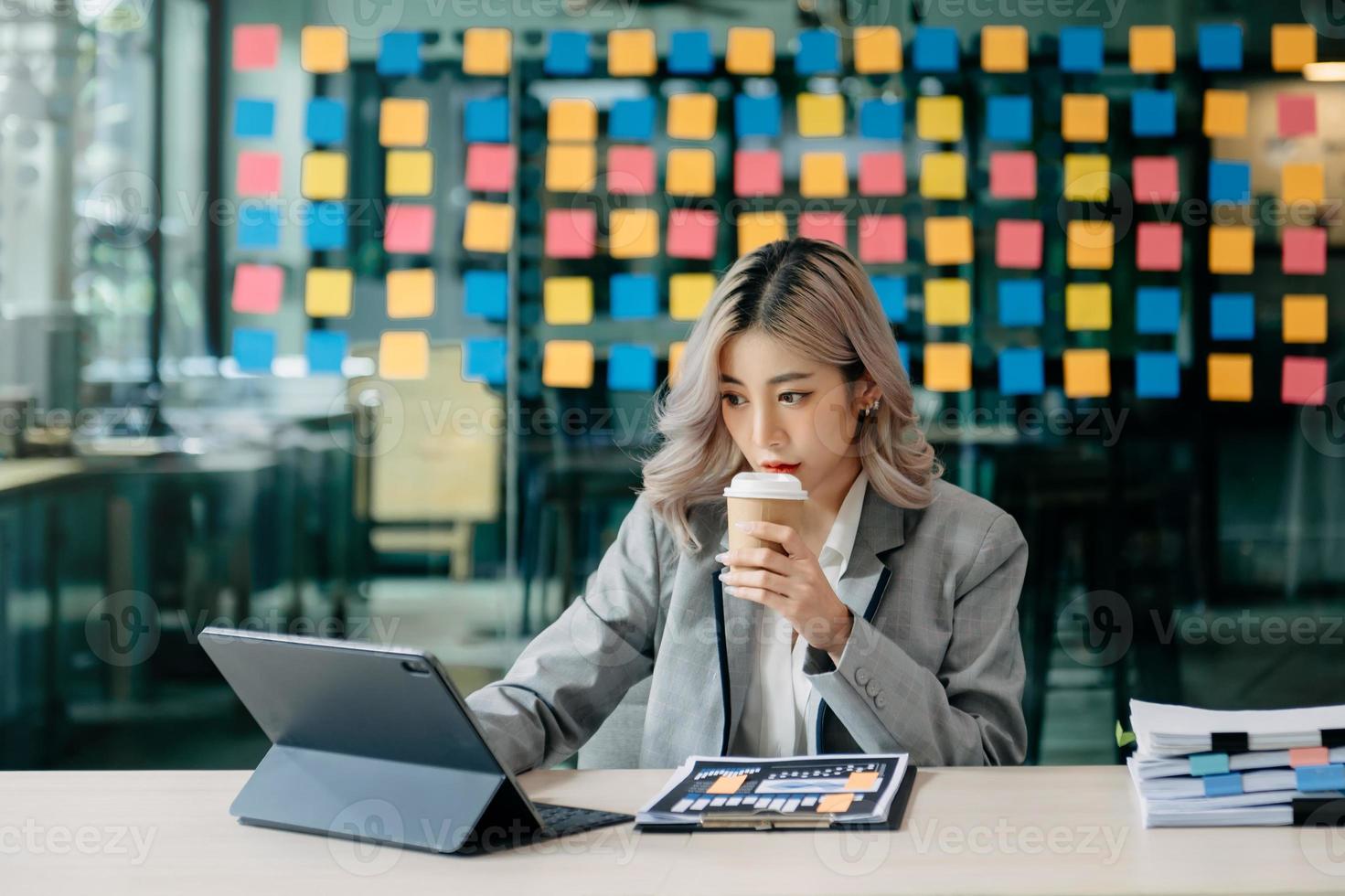 confiada hermosa mujer de negocios asiática escribiendo computadora portátil y tableta digital mientras toma café en la oficina foto