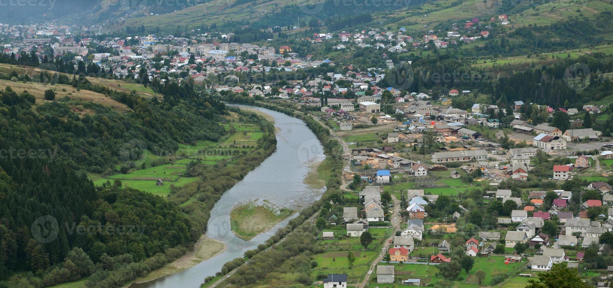 A beautiful view of the village of Mezhgorye, Carpathian region. A lot of residential buildings surrounded by high forest mountains and long river photo