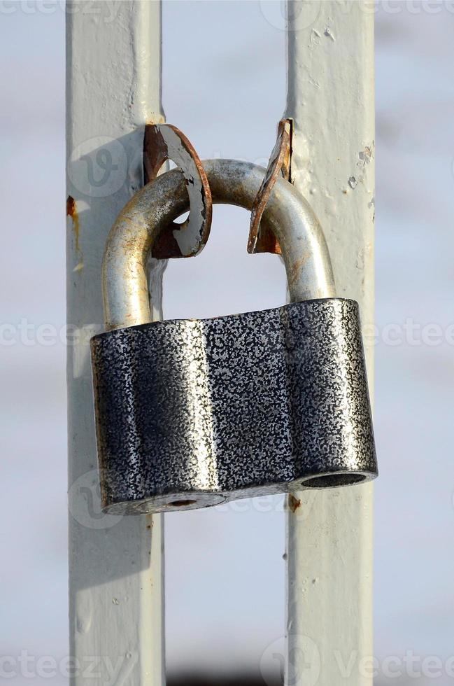 A large gray padlock hangs on a metal gate photo