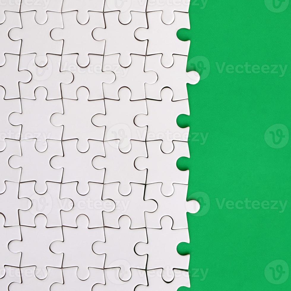 Fragment of a folded white jigsaw puzzle on the background of a green plastic surface. Texture photo with copy space for text