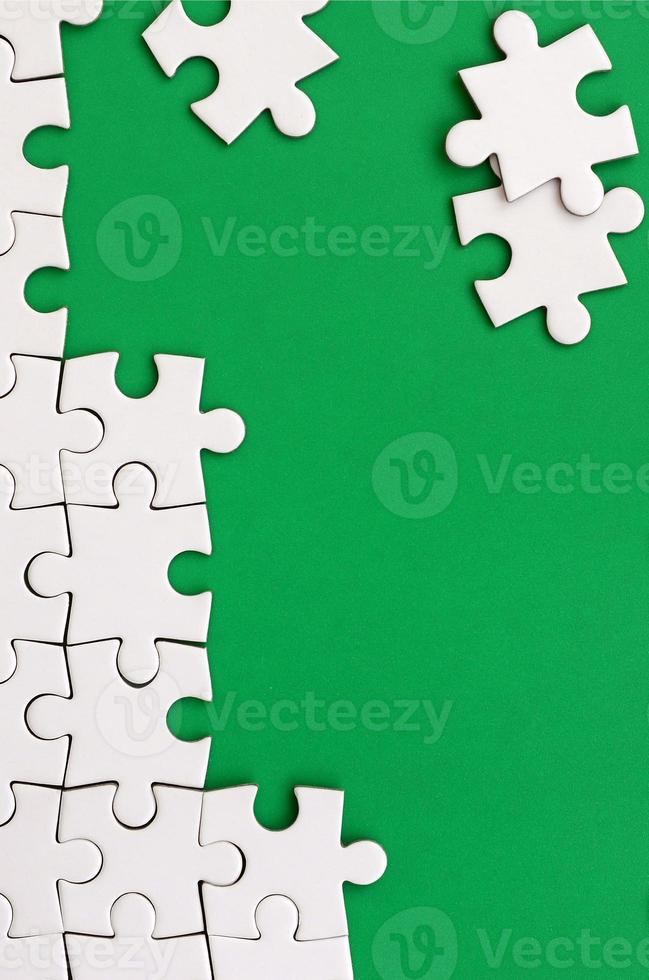 Fragment of a folded white jigsaw puzzle and a pile of uncombed puzzle elements against the background of a green surface. Texture photo with space for text