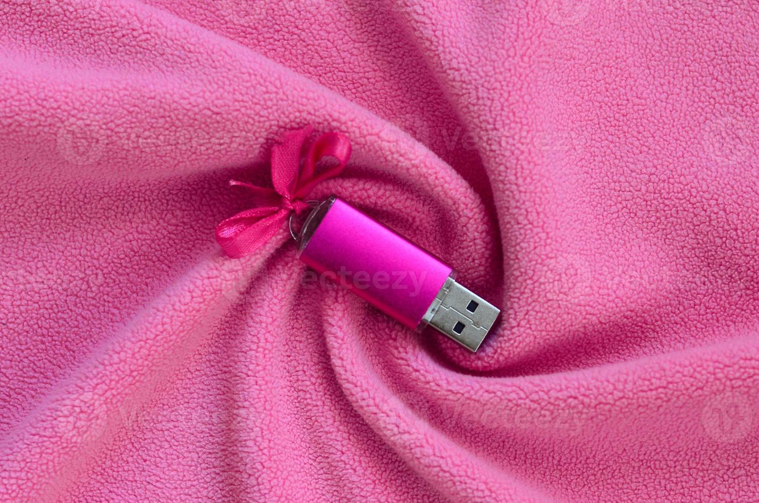 Brilliant pink usb flash memory card with a pink bow lies on a blanket of soft and furry light pink fleece fabric with a lot of relief folds. Memory storage device in women's design photo