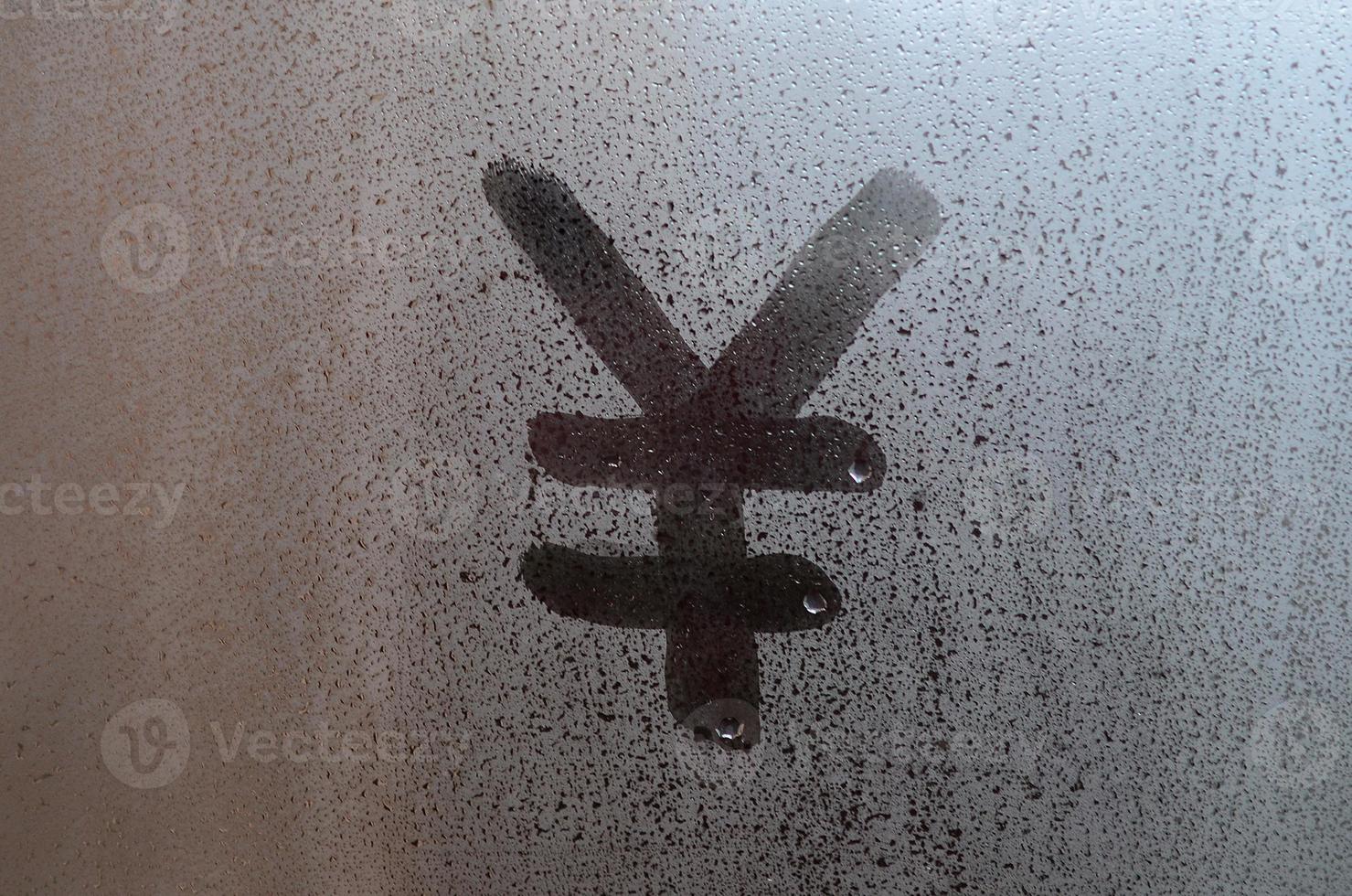 Chinese Yen Symbol is written with a finger on the surface of the misted glass photo