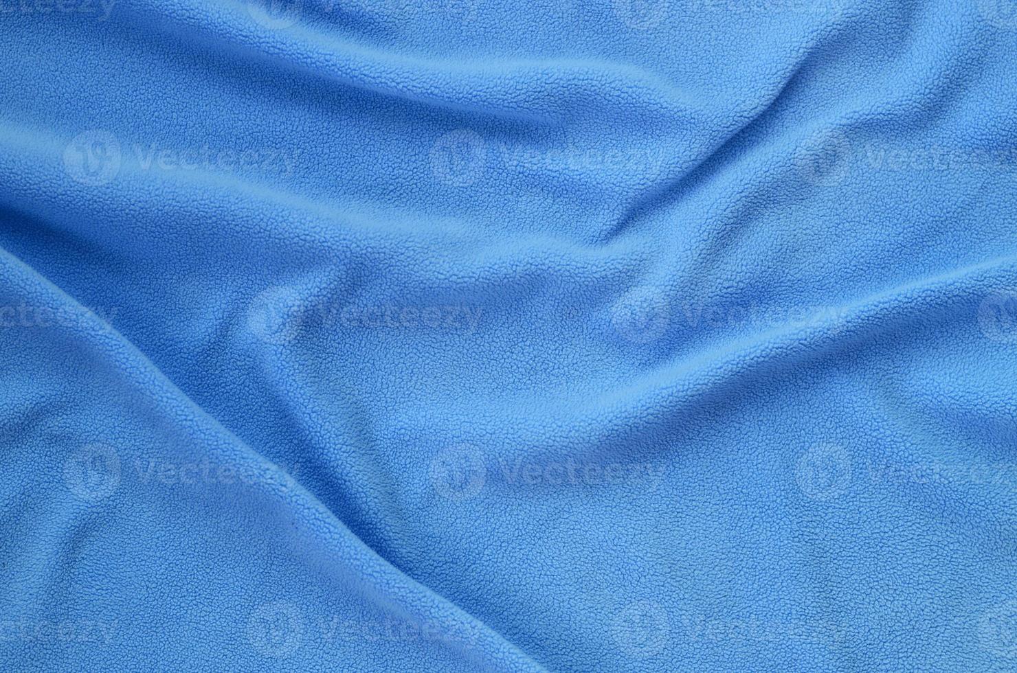 The blanket of furry blue fleece fabric. A background of light blue soft plush fleece material with a lot of relief folds photo