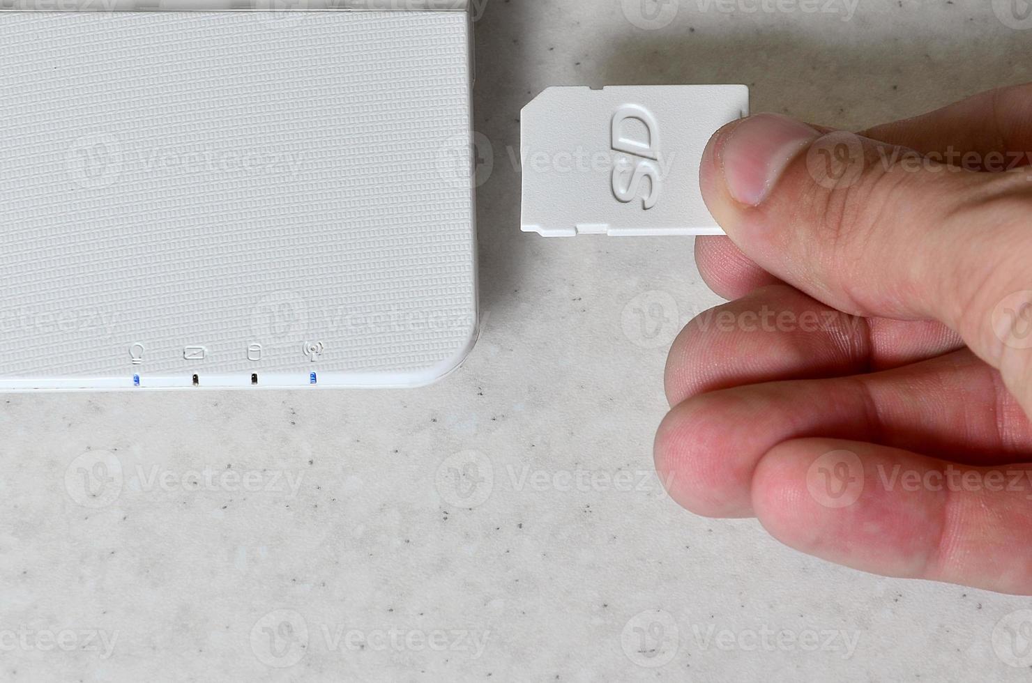 A male hand inserts a white compact SD card into the corresponding input in the side of the white netbook. Man uses modern technologies to store memory and digital data photo