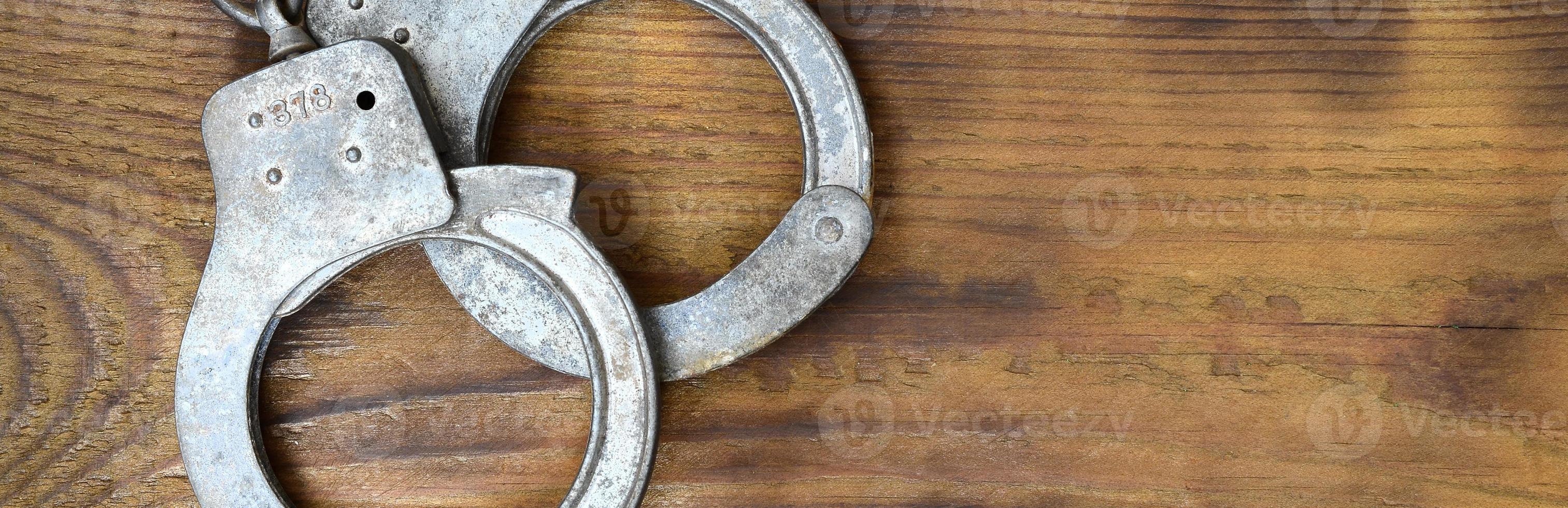 Old and rusty police handcuffs lie on a scratched wooden surface. The concept of an old crime photo