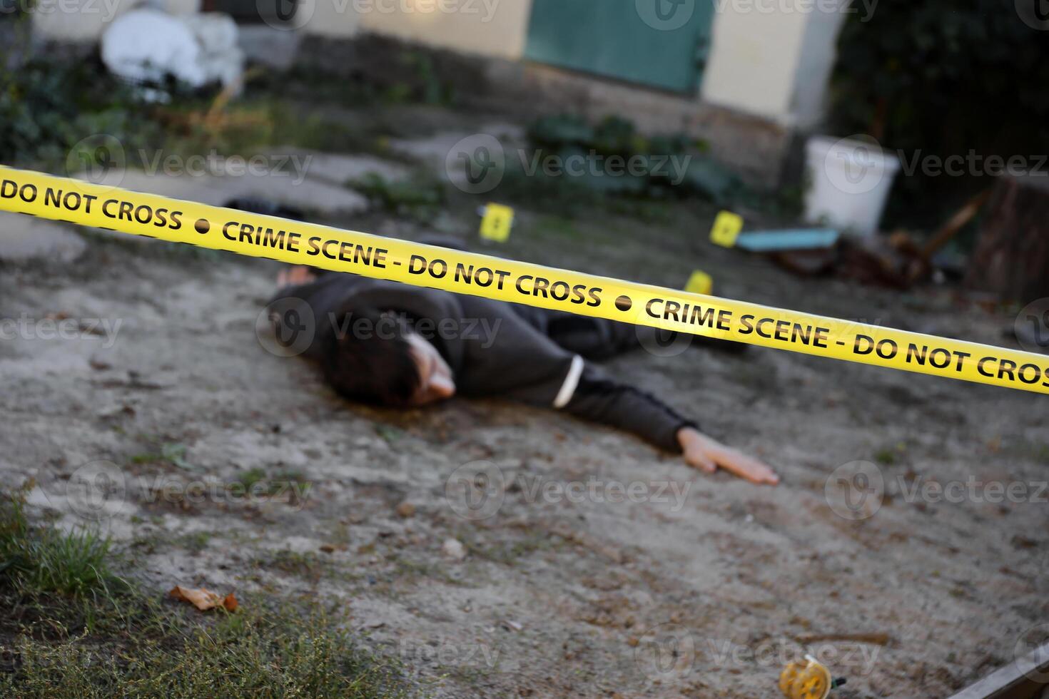 Victim of a violent crime in a backyard of residental house in evening. Dead man body under the yellow police line tape and evidence markers on crime scene photo