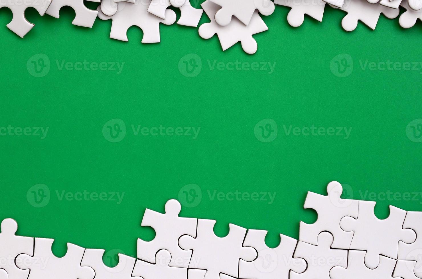 Fragment of a folded white jigsaw puzzle and a pile of uncombed puzzle elements against the background of a green surface. Texture photo with space for text