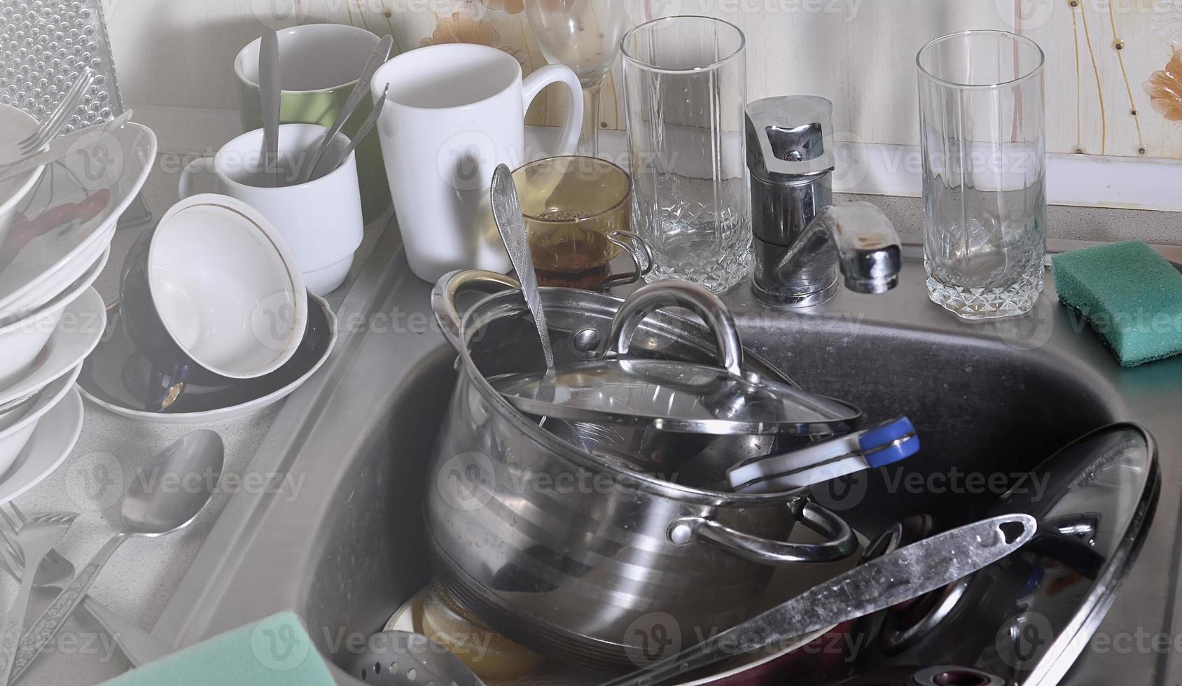 A huge pile of unwashed dishes in the kitchen sink and on the countertop photo