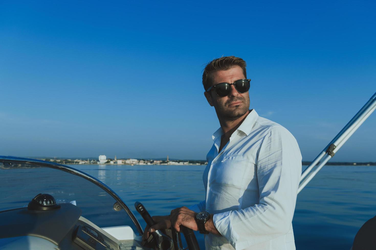 A determined senior businessman in casual clothes and sunglasses enjoys his vacation driving a luxury boat at sunset. Selective focus photo