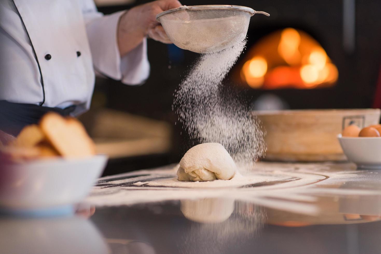 chef sprinkling flour over fresh pizza dough photo