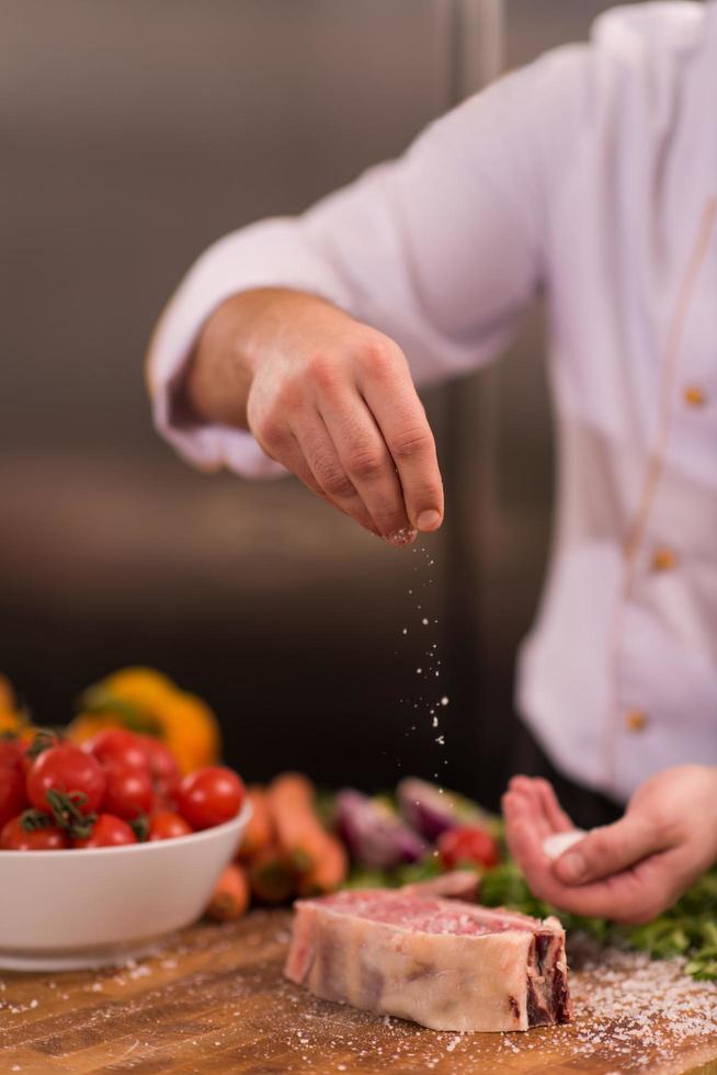 chef poniendo sal en una jugosa rebanada de bistec crudo foto